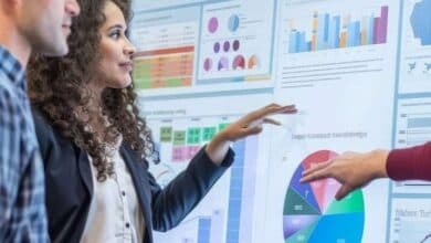 Una donna e un uomo osservano un grosso schermo sul quale vengono proiettati dati e statistiche