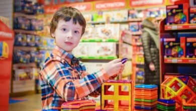 Bambino con capelli neri e camicia di flanella gioca con delle costruzioni colorate