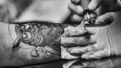 Tatuatore disegna un gufo sul braccio di un cliente