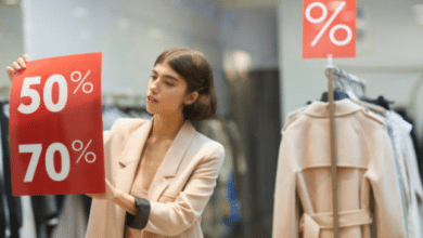 Giovane donna con capelli a caschetto e blazer havana appende un cartello di sconti sulla vetrina del negozio